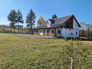 ein weißes Haus mit einem Baum auf einem Feld in der Unterkunft Vama Buzaului Hillside Barn - camere la munte in Vama Buzăului