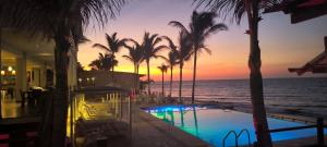 a pool with palm trees and the ocean at sunset at Hotel Punta del Mar in Máncora Chico