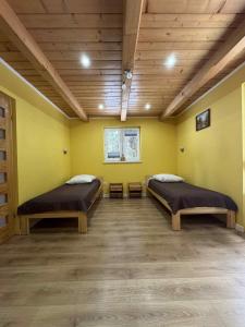 two beds in a room with yellow walls and wooden ceilings at Ośrodek Nad Potokiem in Poręba Wielka