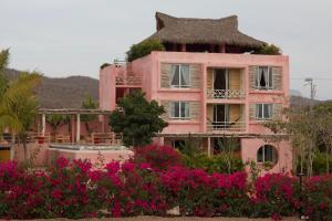 an old pink house with a grass roof and pink flowers at Chamela Boutique Apartments in Chamela