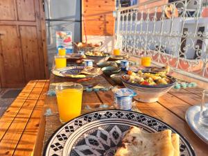 a wooden table topped with plates of food and orange juice at Tawja Surf House in Taghazout +43 photos