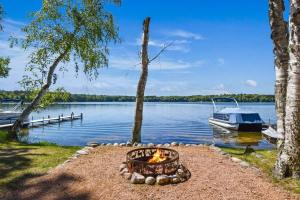 a fire pit next to a lake with a boat at Whispering Waters Bayview Resort Cabin 4 in Saint Germain +23 photos