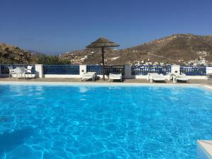 a large blue swimming pool with chairs and an umbrella at Rita's Place Hotel in Ios Chora