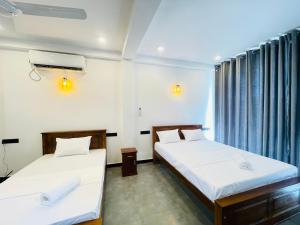 two beds in a room with blue curtains at Yehara Apartments in Weligama