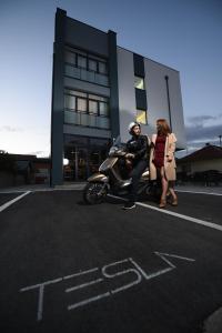 Un uomo seduto su una moto di fronte a un edificio di Hotel Tesla a Banja Luka