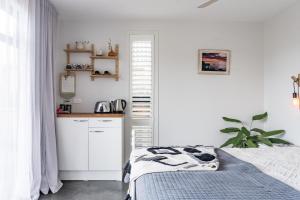 a white bedroom with a bed and a kitchen at Walnut Studio in Raglan