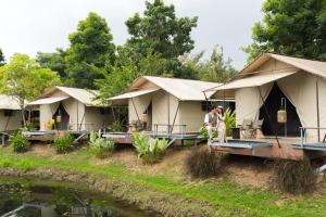 two people standing in front of tents next to a river at The Tree Riverside Resort Kaeng Krachan in Kaeng Krachan
