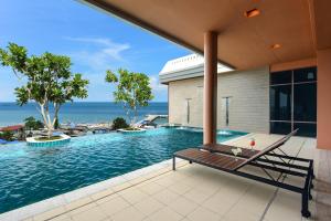 uma piscina exterior com um banco e o oceano ao fundo em Hisea Huahin Hotel em Hua Hin