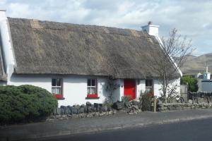 a white house with a thatched roof and red doors at Rockmount House B&B in Clifden