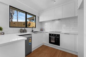 a white kitchen with white appliances and a window at Henderson Oasis in Auckland +2 photos