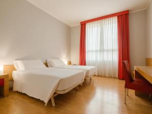 a bedroom with two beds and a window with red curtains at B&B HOTEL Remilia in Reggio Emilia