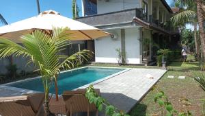 a swimming pool with an umbrella next to a house at Asli Bali Homestay in Candidasa