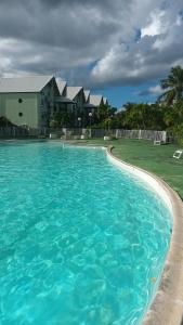 a large blue swimming pool with houses in the background at Une terrasse pleine vue mer in Le Gosier