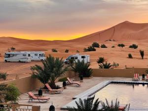 a view of a desert with two rvs and a pool at Hotel Camping Les Roses Des Dunes & Piscine in Merzouga