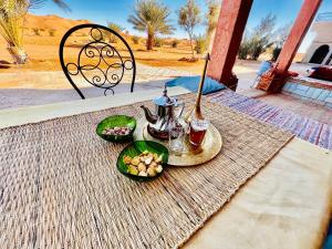 a table with two plates of food and a tea kettle at Hotel Camping Les Roses Des Dunes & Piscine in Merzouga