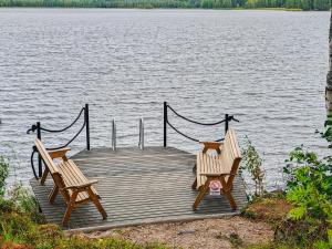 two wooden benches sitting on a dock on a lake at Holiday Home Saarenpää by Interhome in Koivisto