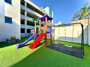 a playground in front of a building with a slide at Apto em Barra Velha 340m da PRAIA com SACADA com CHURRASQUEIRA, AR CONDICIONADO WI-FI, PISCINA, PORTARIA 24h, ACADEMIA MINI MERCADO e vaga de GARAGEM in Barra Velha