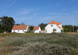 a white house with red roofs in a field at Løkken Klit Camping & Cottage Village in Løkken