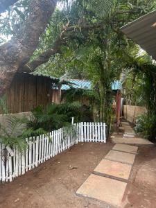 a white picket fence in front of a fence with trees at Prakriti Resort in Arambol