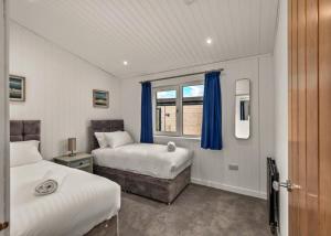 a bedroom with two beds and a window with blue curtains at Finest Retreats - Silverwood Deluxe Chalet in Errol
