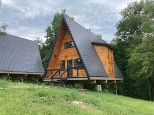a wooden house with a black roof on a hill at Dogwood Den- Cozy Forest A-Frame Near Bentonville in Rogers