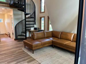 a leather couch in a living room with a staircase at Black Gum Getaway-Cozy Forest A-frame Near Bentonville in Rogers