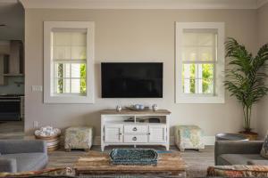 a living room with a tv on a wall with two windows at Springtide House -Dock & Home w Pool in Stock Island