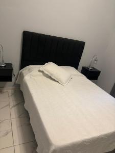 a large white bed with a black headboard and two lamps at Hospedaje Adha Chivilcoy III in Chivilcoy