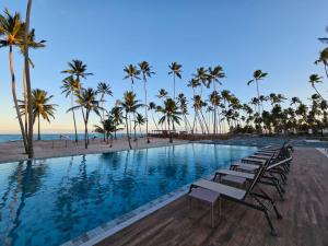 a pool with chairs and palm trees on the beach at Apartamento Ipioca Beach Life in Ipioca