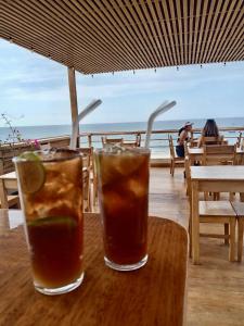 two drinks on a wooden table with a view of the ocean at PUNTA VELEROS ROOFTOP in Los Órganos