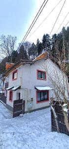 a white house with red windows in the snow at Casa Kati in Buşteni
