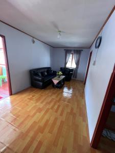 a living room with a black couch and a wooden floor at Homestay Natasya in Pohe