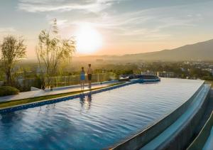two people standing on the edge of a swimming pool with the sunset at Astra Sky River Chang Khlan Chiang Mai in Chiang Mai