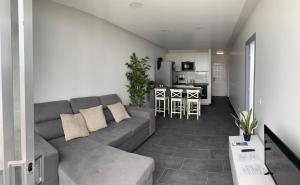 a living room with a gray couch and a kitchen at Pandora apartment in Las Galletas