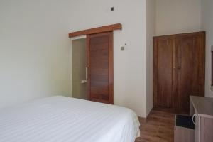 a bedroom with a white bed and a wooden door at Rumah Kecil kesari in Denpasar