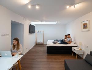 three people sitting on beds in a room with a laptop at Pixel Guesthouse in Târgu Secuiesc