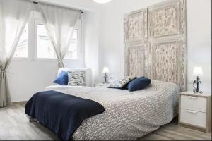 a white bedroom with a large bed with blue pillows at Apartamentos Rivera in Alicante