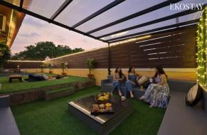 three women sitting on a couch on a patio at EKOSTAY - Pinewood Villa in Alibaug