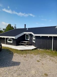 a black house with a picnic table in front of it at Beautiful cottage on a large natural plot in Ålbæk