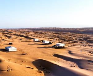 a desert with four white structures in the sand at Aurora desert camp in Badīyah