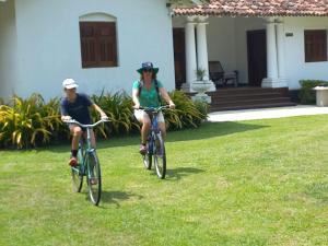 two people riding bikes on the grass in front of a house at Tamarind Villa in Kelaniya