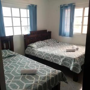 two beds in a bedroom with blue curtains and windows at Right Lang Deh Soh in San Andrés
