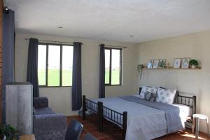a bedroom with a bed and a chair and windows at Hermosa habitación de campo in San Gregorio Atzompa