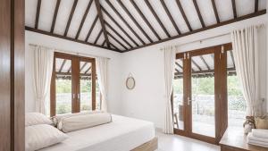 a bedroom with a bed with white sheets and windows at Lonovilla Menoreh Yogyakarta in Junggrangan