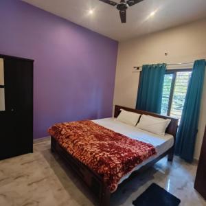 a bedroom with a bed with purple walls and a window at Golden Valley Abode in Siddapur