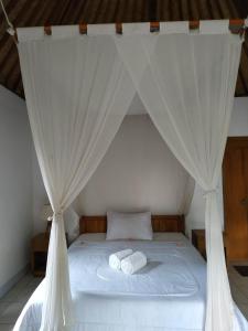 a bed with white curtains and two towels on it at The Bukit Artha in Sidemen