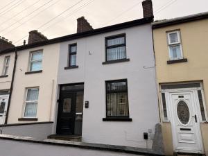 a white house with a black door on a street at 2 Bedroom House By Travel Lets Holiday Homes Derry With Garden in Derry Londonderry