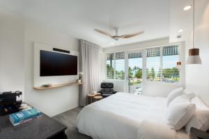 a white bedroom with a large bed and a tv at Heart Hotel and Gallery Whitsundays in Airlie Beach