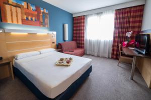 トリノにあるイデア ホテル トリノ ミラフィオリのベッド、椅子、テレビが備わるホテルルームです。