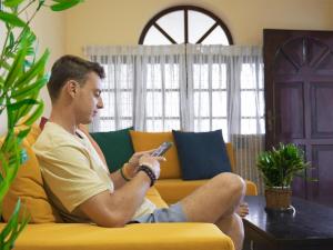 a man sitting on a couch holding a cell phone at 2in1 Kandy Hostel in Kandy